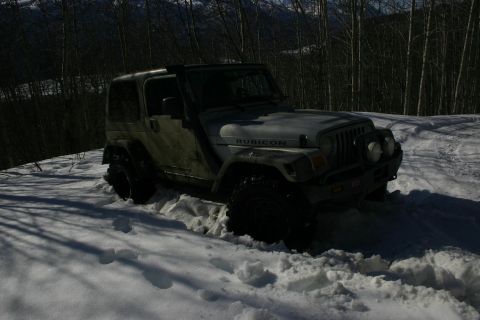 2003 Jeep TJ - A silver Jeep TJ Rubicon is partially submerged in deep snow, with trees and mountains in the background.