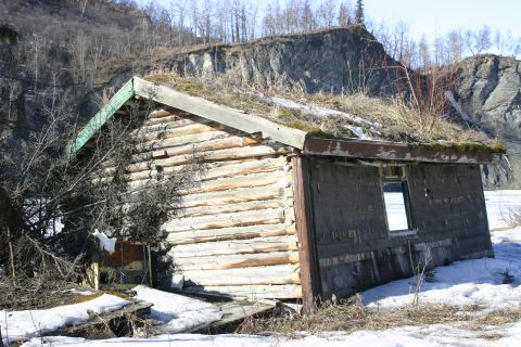 2003 Jeep TJ - An old log cabin sits abandoned in a snowy landscape, with vegetation growing on its roof.