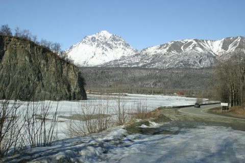 2003 Jeep TJ - A lone SUV navigates a snow-dusted road through a scenic winter landscape with mountains and a frozen river.