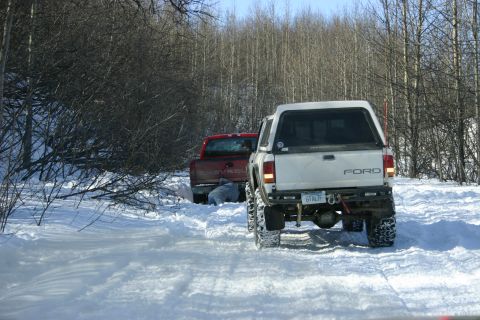 2003 Jeep TJ - Two trucks are stuck in the snow on a trail, with one person appearing to be working on the red truck.