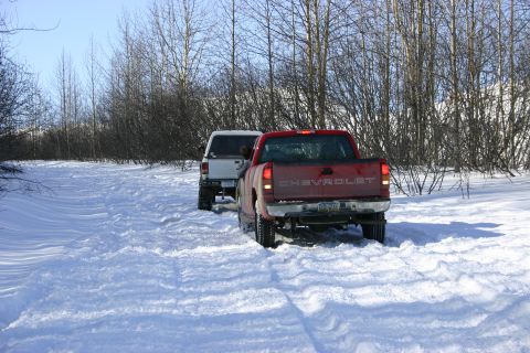 2003 Jeep TJ - Two trucks navigate a snowy path, with the red Chevrolet pickup leading the way.
