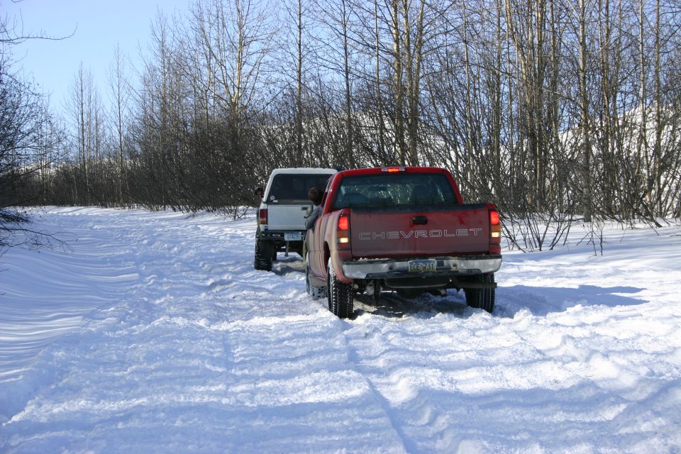 Red Chevrolet pickup truck rear view in snow, followed by white SUV