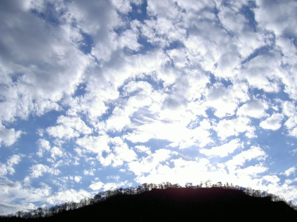 Cloud-filled blue sky over a silhouetted tree-covered hill