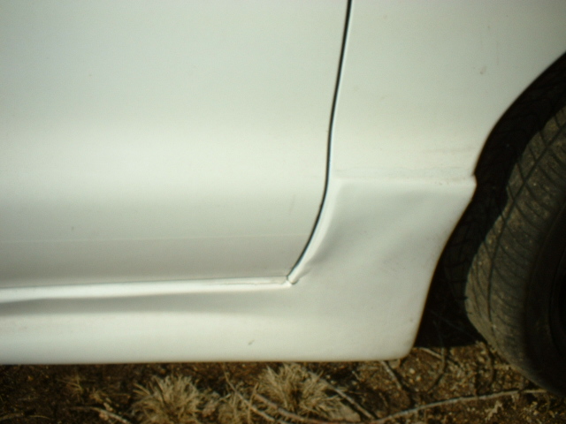 White car's side door and rocker panel with a visible seam and a tire on the right