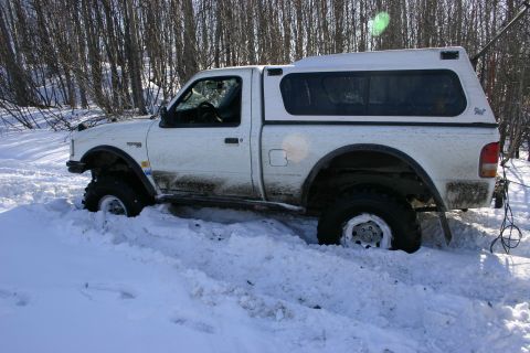 2003 Jeep TJ - A white pickup truck is stuck in the snow, with its tires buried deep.
