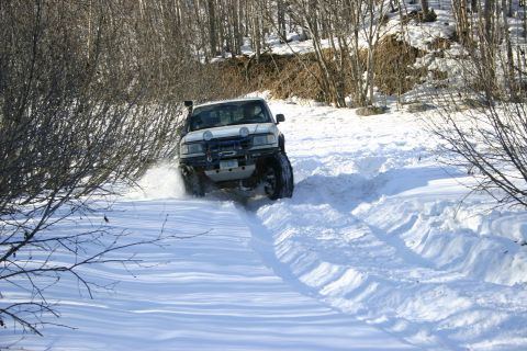 2003 Jeep TJ - A white SUV navigates a snow-covered trail with trees in the background.