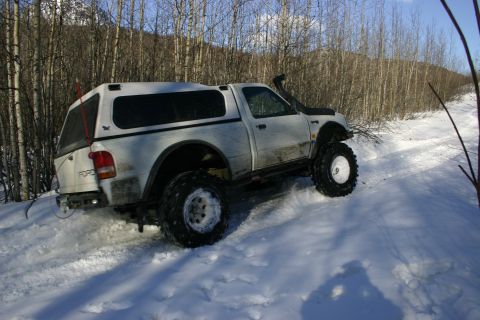 2003 Jeep TJ - Modified Ford pickup truck navigates a snowy trail with a snorkel and camper shell.