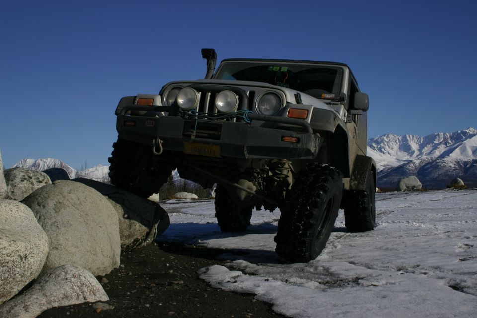 Silver Jeep TJ with snorkel and off-road tires climbing over rocks on a snowy landscape