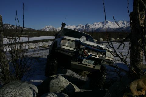 2003 Jeep TJ - A white off-road vehicle navigates a rocky path with snow-capped mountains in the background.