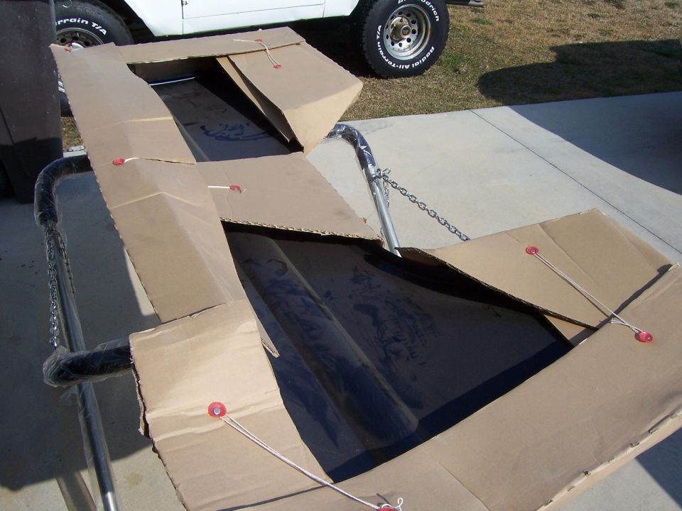 cardboard box with a black car part inside, white vehicle in background