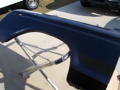 1978 Ford Bronco - A freshly painted dark navy blue front fender panel with wheel arch and side marker light cutout, laid face-up on a concrete driveway. A ch…