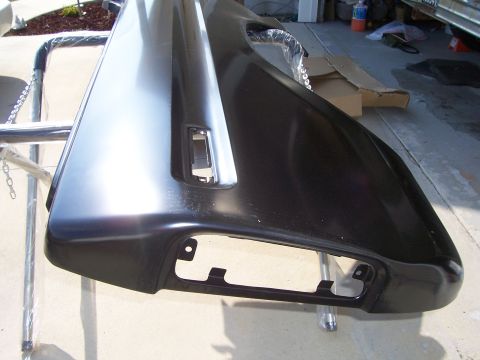 1978 Ford Bronco - A new dark-painted quarter panel skin resting on chrome tubing in a driveway, viewed from the rear corner with its rectangular tail-light o…