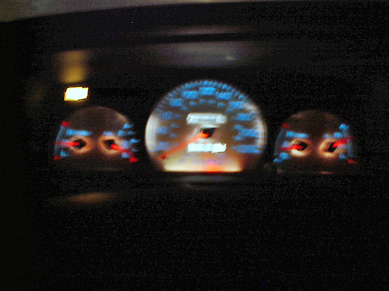 Dashboard gauges with blue illumination and a digital odometer reading 123456. A yellow warning light is visible