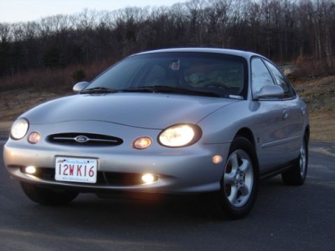 1999 Ford Taurus - This sedan is parked on a road with a wooded area behind it.