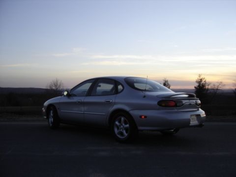 1999 Ford Taurus - A silver sedan is parked on the side of the road during sunset.