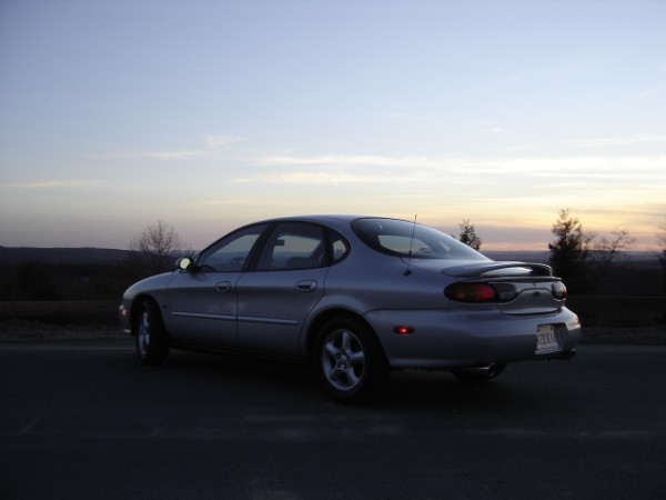 Silver sedan parked on a road at dusk. The car has a spoiler on the trunk