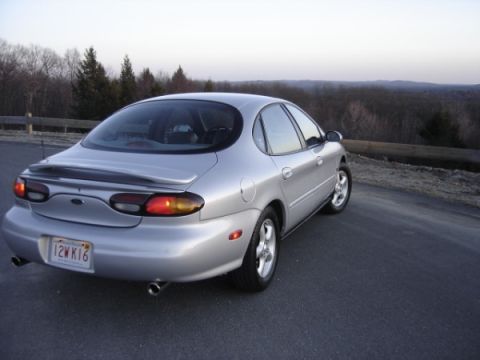 1999 Ford Taurus - Rear view of a silver 1999 Ford Taurus sedan parked on a road overlooking a wooded landscape.