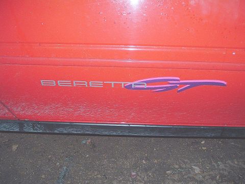 1991 Chevrolet Beretta - Close-up of a red car's side door, showing the 'BERETTA GT' emblem with a purple graphic.