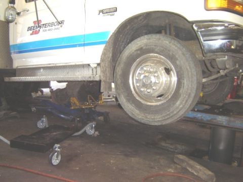 1992 Ford Bronco - A Ford Super Duty truck is being serviced on a lift, with its front wheel removed and a floor jack positioned below.