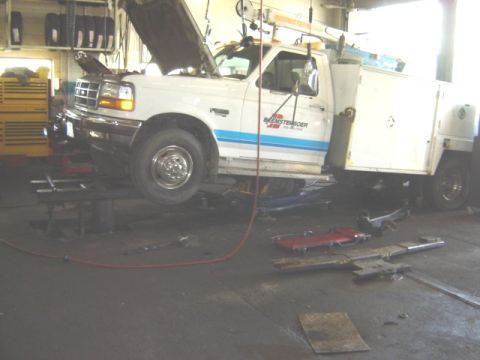 1992 Ford Bronco - A white service truck with a blue stripe is shown with its hood open while elevated on a lift in a garage. The grille indicates it is a 199…