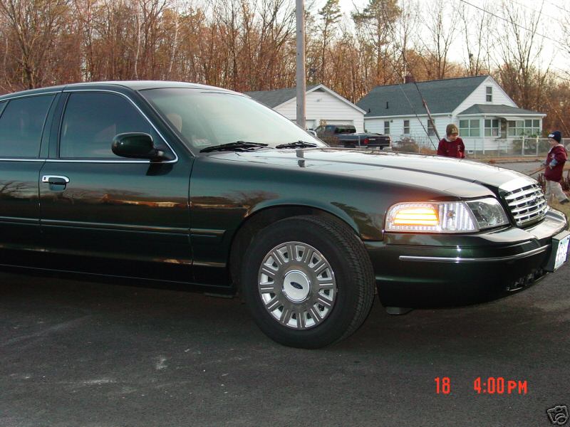 Dark green sedan, possibly a Crown Victoria, parked outside houses. Front quarter view