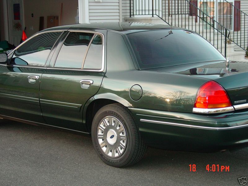Dark green 2003 Ford Crown Victoria sedan, rear quarter view, chrome trim, tinted windows, slight damage on r…