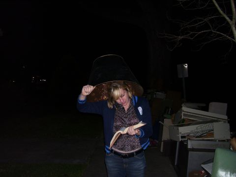 1992 Ford Bronco - Woman with a lampshade hat reads a book in the dark, with discarded items in the background.