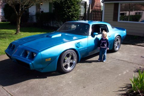 1979 Pontiac Trans Am - A bright blue 1979 Pontiac Trans Am is parked in a residential driveway, with a small child standing beside it.