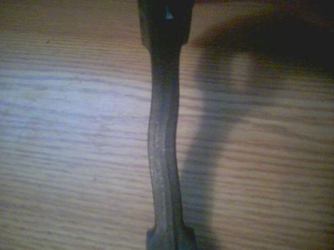 1996 Ford Probe - A bent metal connecting rod lies on a wooden surface, indicating mechanical damage.