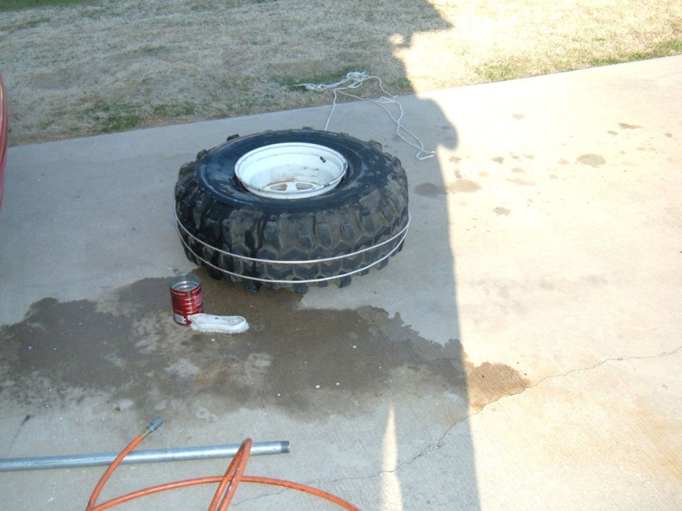 Tire and rim on concrete with a can of paint and a brush nearby
