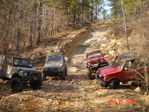 1978 Ford Bronco - Several Suzuki Samurai SUVs navigate a challenging off-road path through a wooded area.