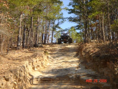 1978 Ford Bronco - An off-road vehicle navigates a steep, rocky trail through a wooded area.