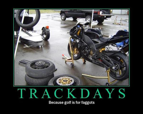 Black sport motorcycle on a stand, with stacked tires and a trailer in the background