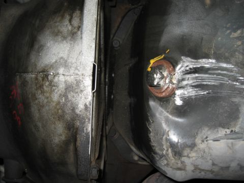 2000 Jeep TJ - The underside of a vehicle shows a fuel tank with a damaged cap and a differential housing.