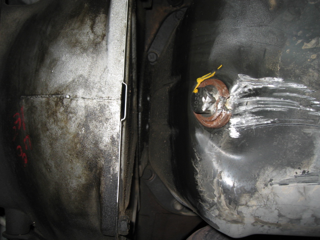 Underside view of a vehicle's fuel tank with a dented cap and a differential housing