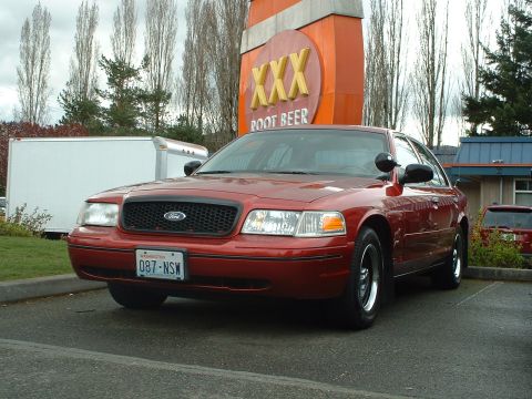 1999 Ford Crown Victoria - Red Ford Crown Victoria parked in front of a XXX Root Beer sign.