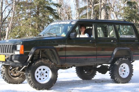 1995 Jeep Cherokee - A lifted Jeep Cherokee sits in a snowy, wooded area with a person inside.