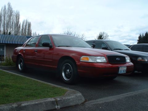 1999 Ford Crown Victoria - A red sedan is parked next to a black car under an overcast sky.
