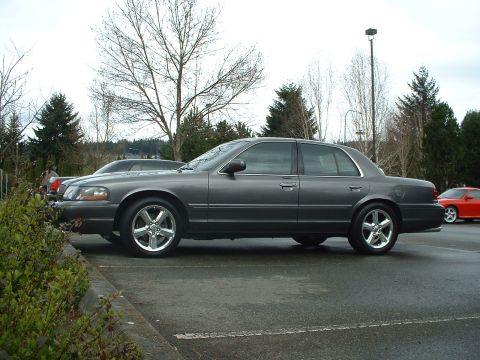 1999 Ford Crown Victoria - A dark gray sedan is parked on a wet asphalt lot, with another vehicle visible in the background.