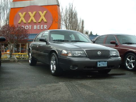 1999 Ford Crown Victoria - Gray Ford Crown Victoria parked outside a XXX Root Beer establishment with another vehicle behind it.
