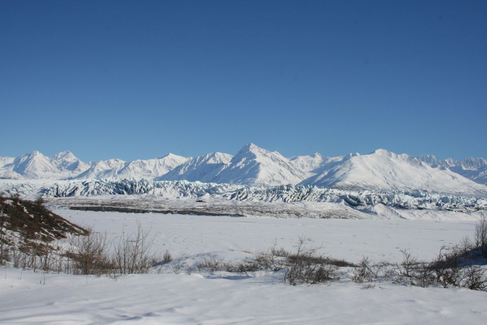 Snow-covered mountain range and glacier under clear blue sky beyond a frozen valley