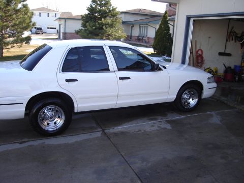 2000 Ford Crown Victoria - Side view of a white sedan with tinted windows and chrome wheels parked on a concrete driveway.