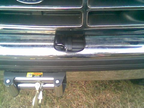 1992 Ford Bronco - Low front view of a dark green Ford truck showing a winch mounted below the chrome bumper, with its yellow warning decal, roller fairlead a…