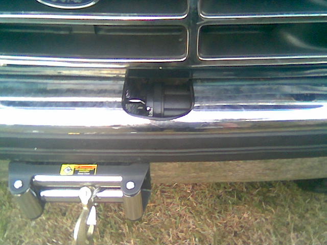 Winch with hook mounted below the chrome front bumper of a dark green Ford truck