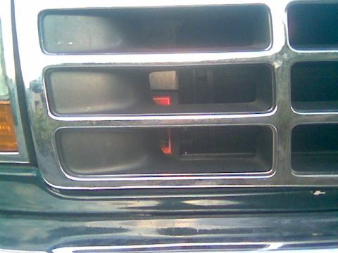 1992 Ford Bronco - Tight close-up of a dark green truck's front grille, showing the chrome-trimmed rectangular slots and a sliver of the amber corner marker l…