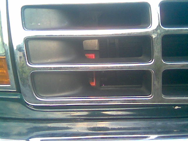 Close-up of dark green truck grille slots with chrome trim and amber marker light at edge
