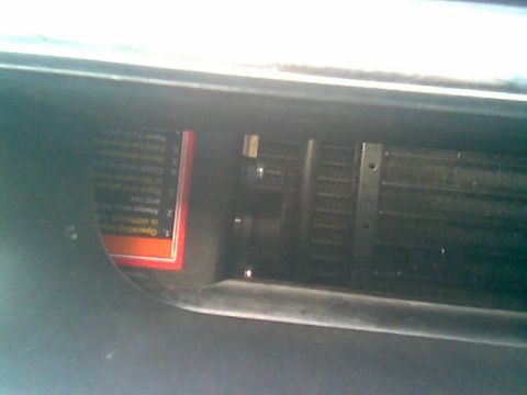 1992 Ford Bronco - Dim close-up of a finned metal heat-exchanger core (radiator or condenser) behind black plastic trim, with an orange-bordered warning label…