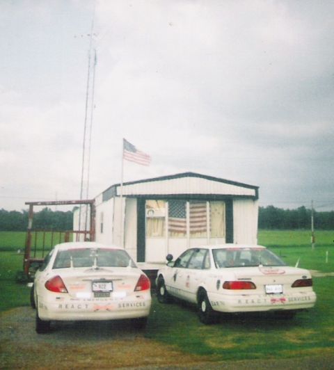 1998 Ford Crown Victoria - Two white sedans with REACT SERVICES markings are parked in front of a trailer under a cloudy sky.