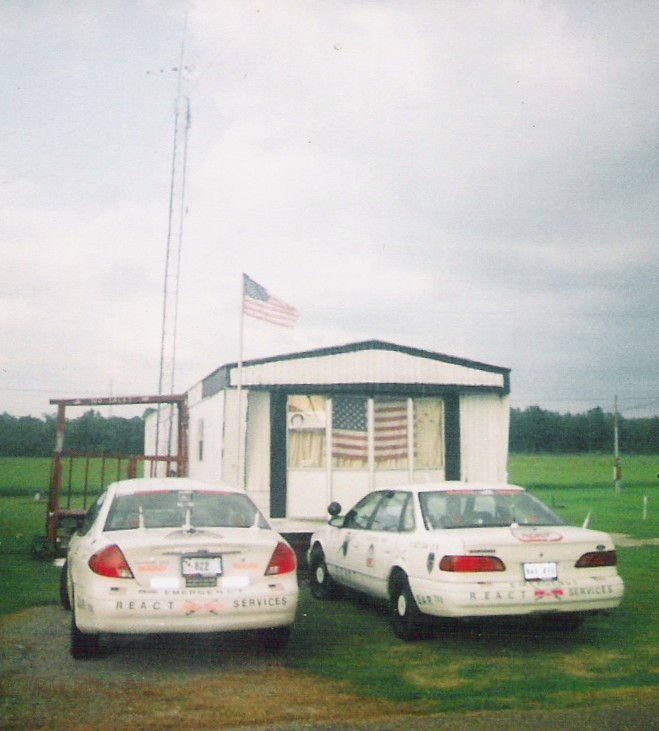 Two white sedans parked in front of a trailer, both have REACT SERVICES text on the rear