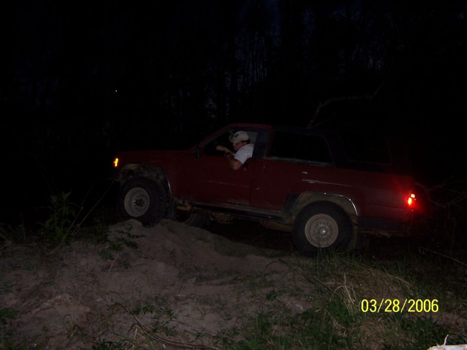 Red SUV driving up a dirt hill at night. Driver is visible